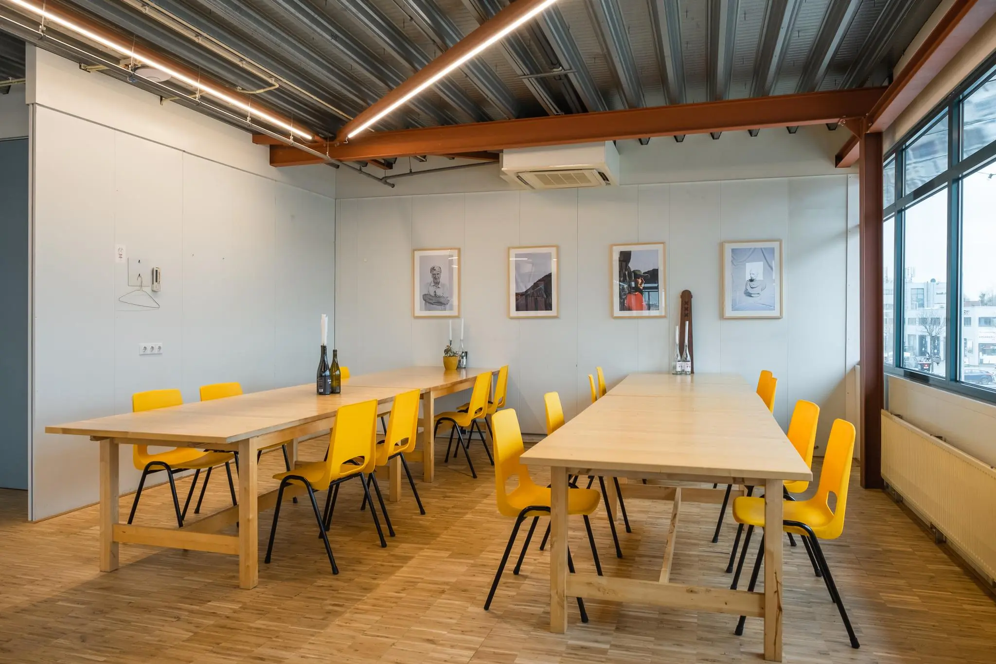 Vergaderruimte aan de Johan van Hasseltweg met lange houten tafels, gele stoelen en kunst aan de muur.